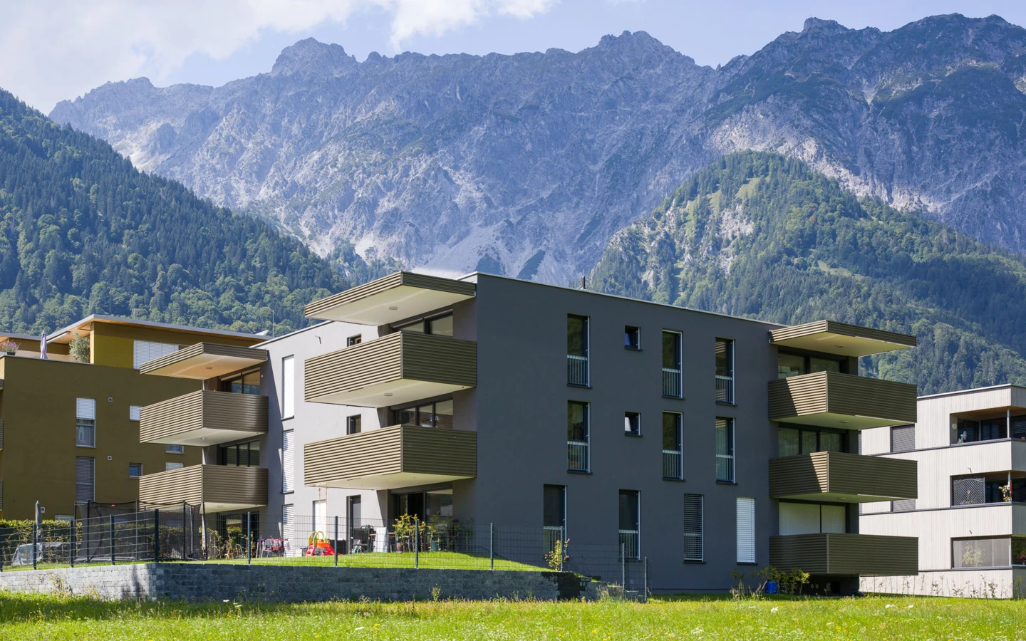 Moderne Wohnanlage mit dunkler und ockerfarbener Fassade und mehreren Balkonen im alpinen Stil in Vandans, umgeben von grünen Bergen und Wiesen (Bahnhofstraße, Bahnhofsstrasse).
