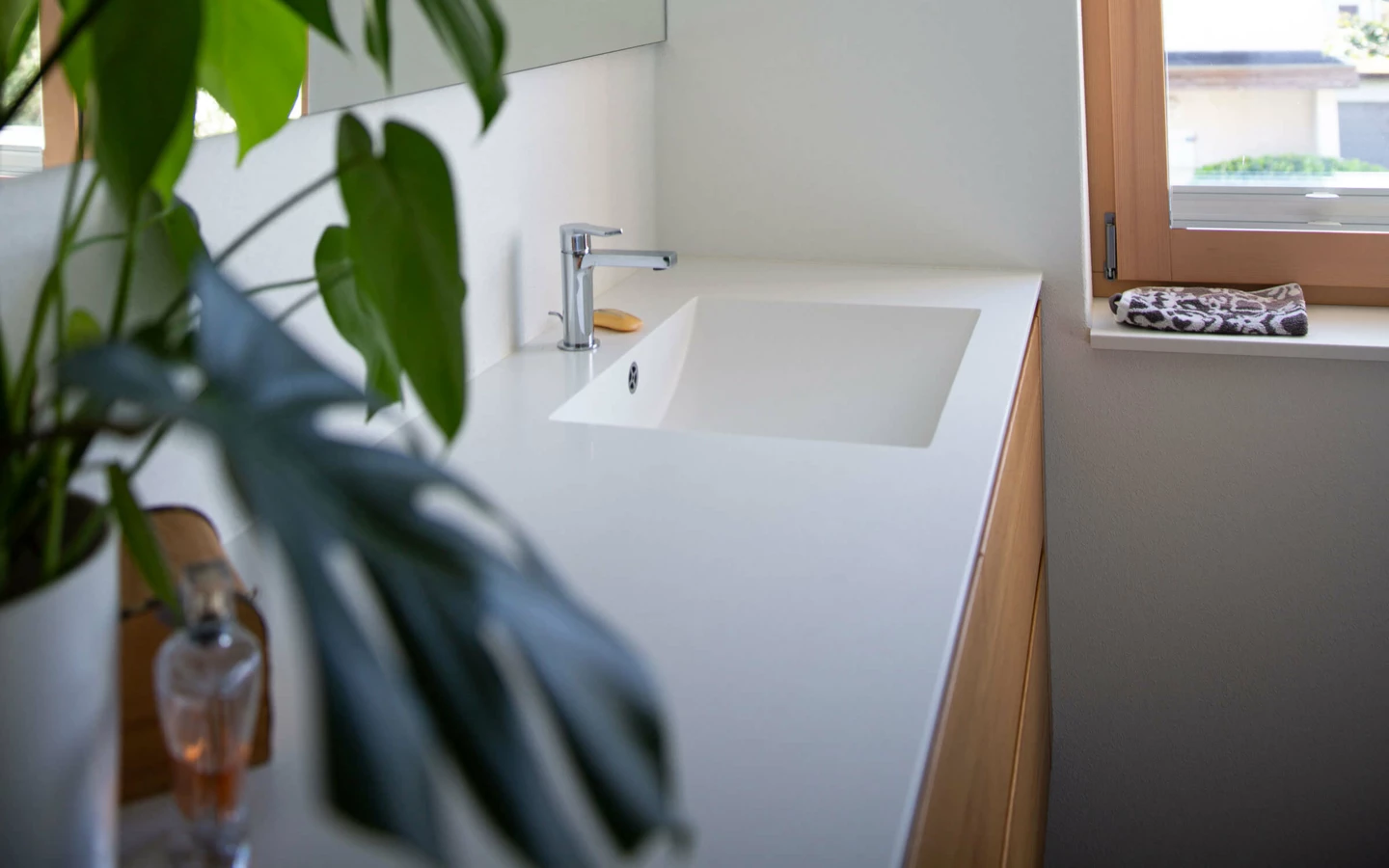 Modernes Badezimmer mit Waschtisch, großem Spiegel, Holzfenster und einer Grünpflanze. Das neue Bad in Dornbirn (Generalsanierung, Einfamilienhaus).