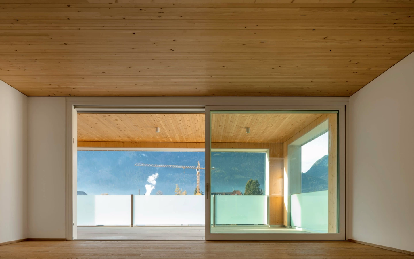 Blick von einem leeren Raum mit Holzboden und Holzdecke auf einen Balkon mit Bergblick (Zürcherstraße, Wohnanlage, Bludenz).