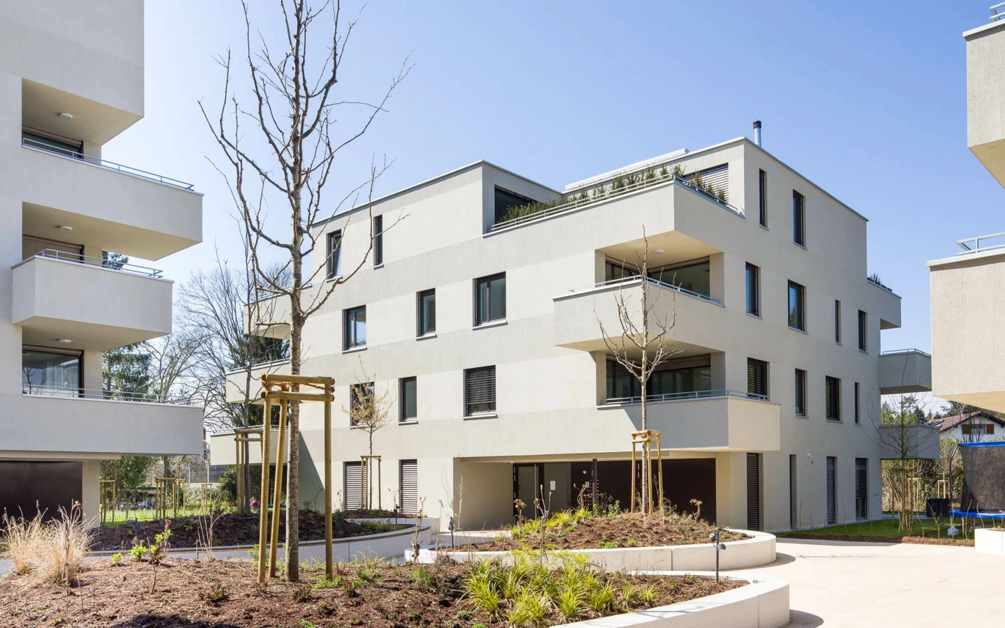 Moderne Wohnanlage mit beigen Fassaden, Balkonen und kleinen Bäumen, umgeben von gepflegten Grünflächen unter blauem Himmel (Wuhrbaumweg).