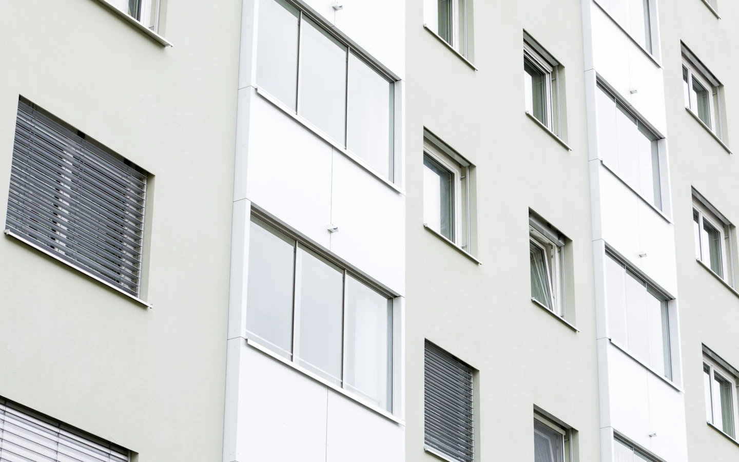 Fassade eines modernen Gebäudes mit hellgrünen Wänden, Fenstern mit Jalousien und gläsernen Balkonen (Römerstraße).