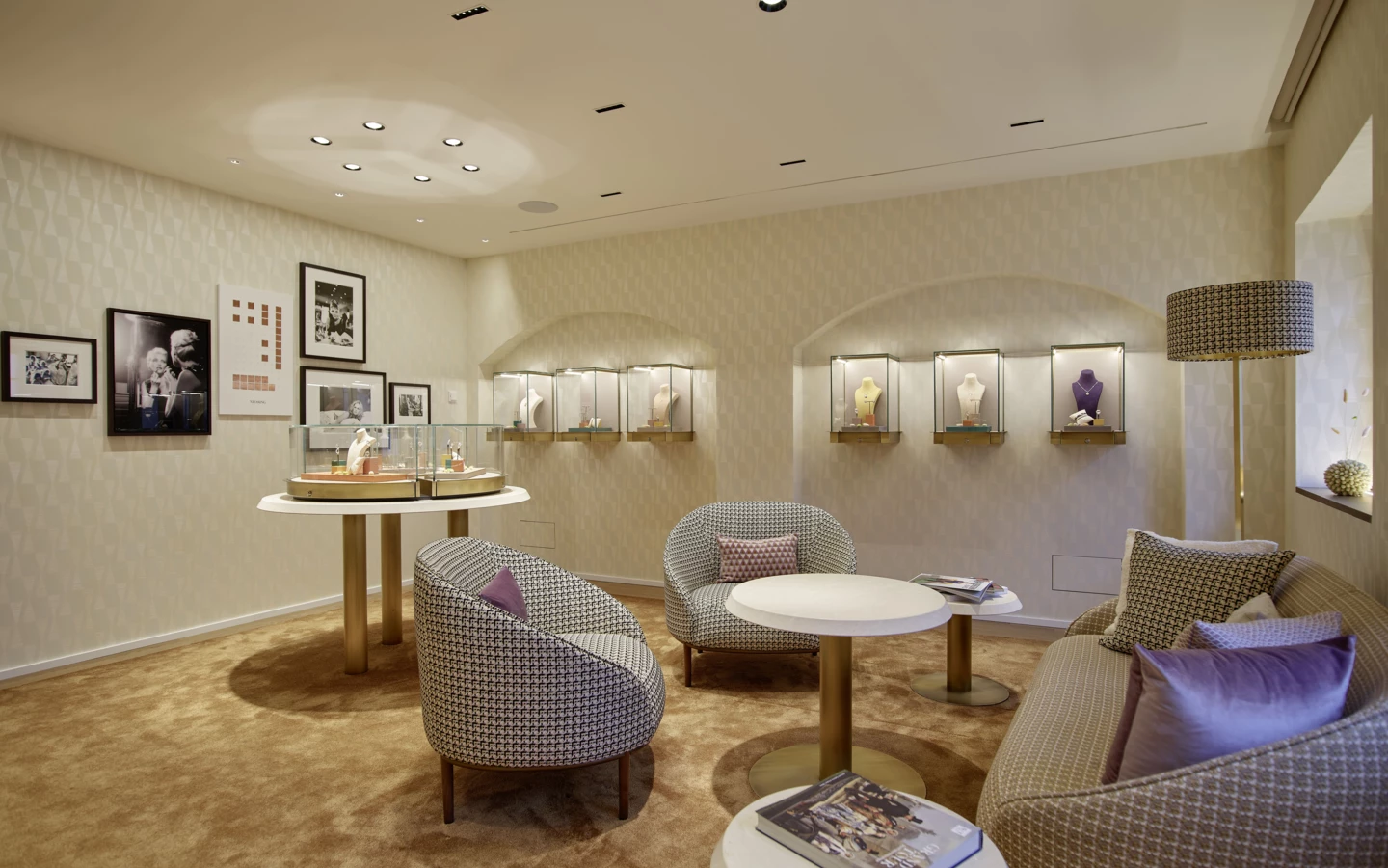 Ein stilvoller Showroom mit Schmuckvitrinen, bequemen Sesseln, runden Tischen und gerahmten Fotos an der gemusterten Wand (Huber, Rathausstr).
