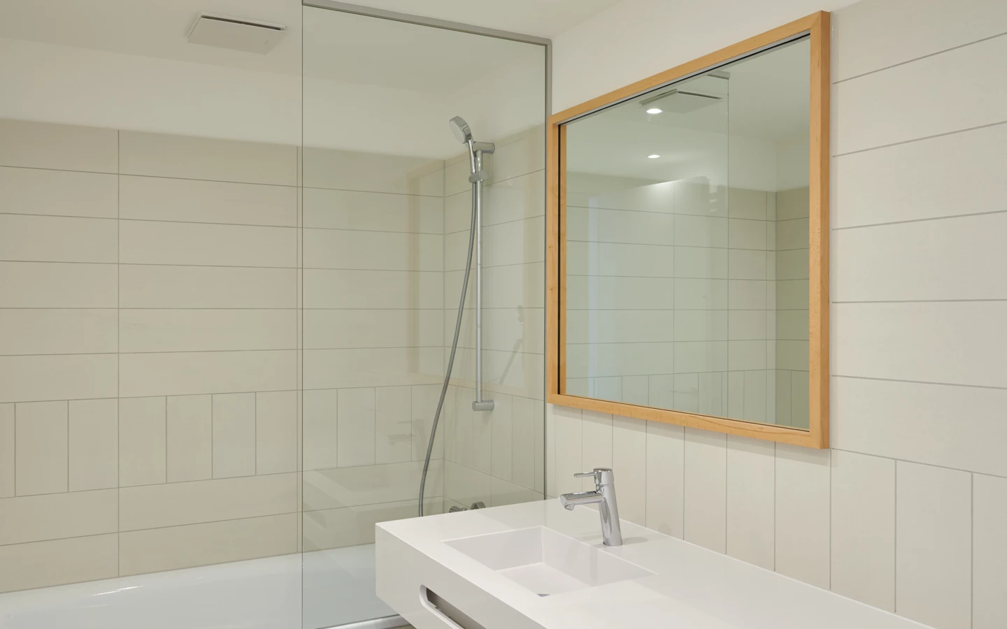 Modernes Badezimmer mit weißer Badewanne, Glasduschabtrennung und einem langen, schwebenden Waschtisch mit Spiegel (Apollogasse).