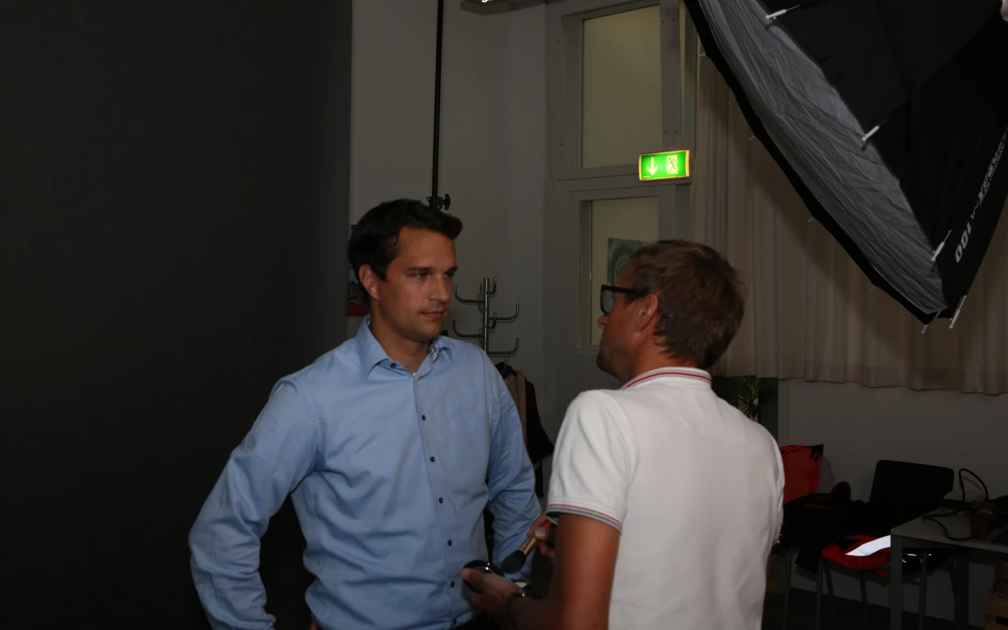 Zwei Männer unterhalten sich bei einem Fotoshooting, ein Softbox-Blitzschirm ist sichtbar.