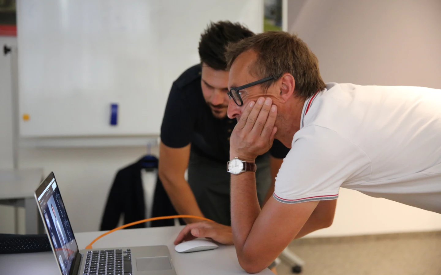 Zwei Männer betrachten konzentriert den Bildschirm eines Laptops auf einem Schreibtisch, einer mit der Hand am Kinn.
