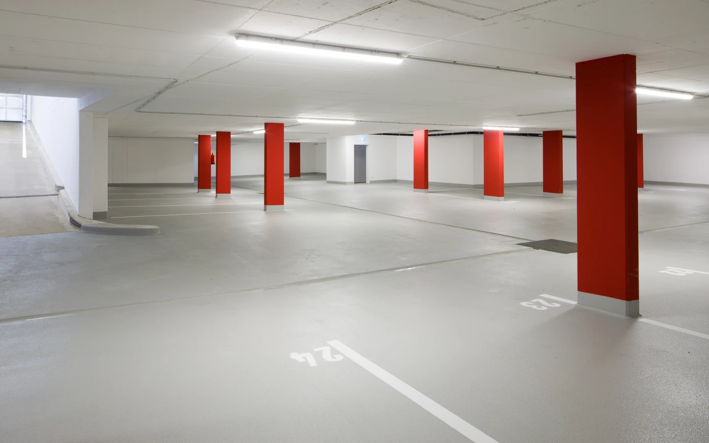 Leere Tiefgarage an der Unterhochstegstraße mit roten Säulen, weißen Parkplatzmarkierungen, hellgrauem Boden und Rampenzufahrt.