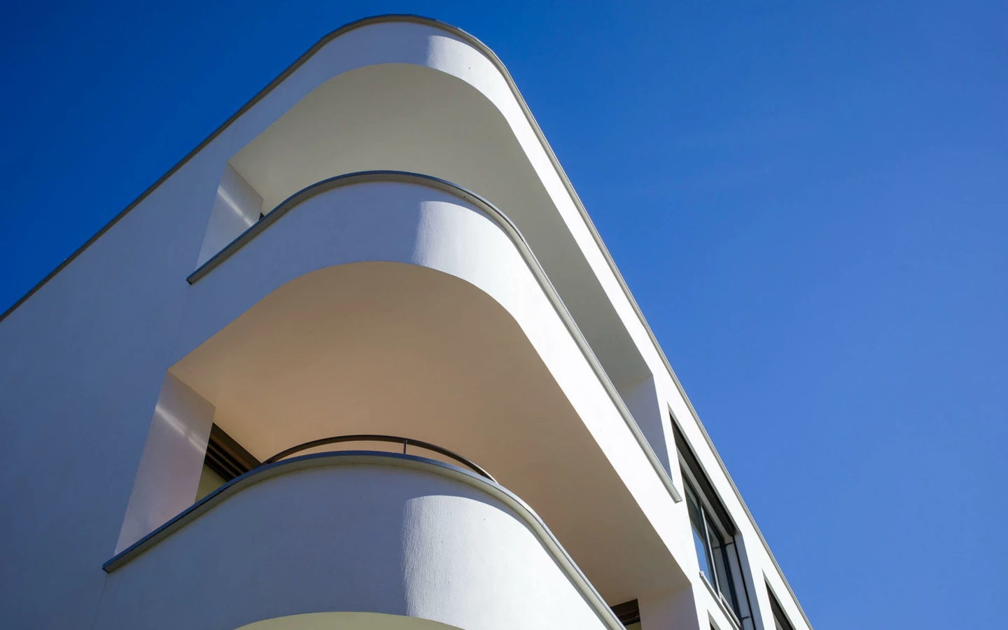 Eine Nahaufnahme der abgerundeten, hellweißen Balkone eines modernen Gebäudes vor einem klaren blauen Himmel bei Tageslicht (Wolf-Huber-Straße, Wohnanlage, Feldkirch).