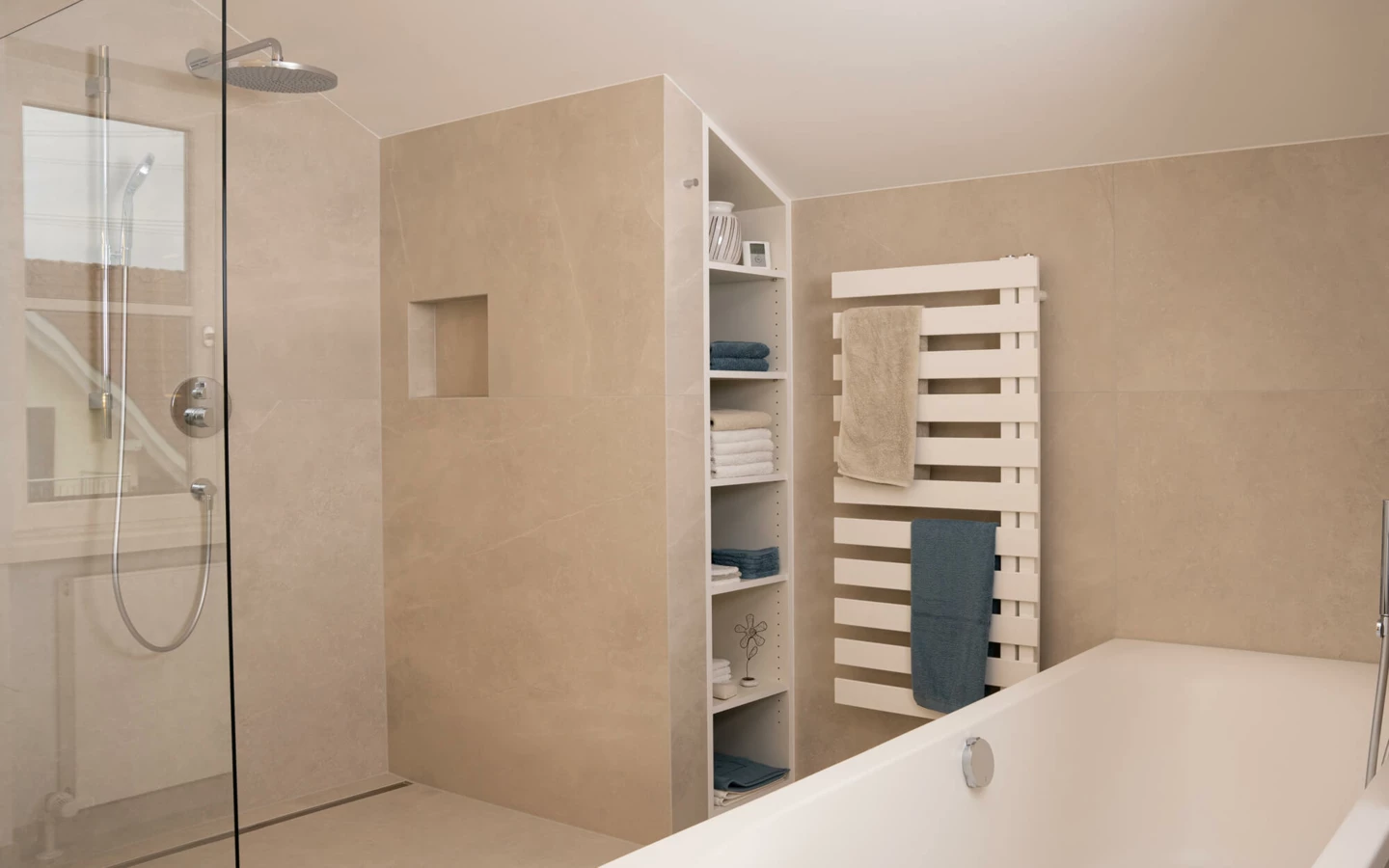 Modernes Bad mit beigen Fliesen, bodengleicher Dusche, Badewanne, Handtuchheizung und Einbauregal mit Handtüchern (Generalsanierung, Bohle).