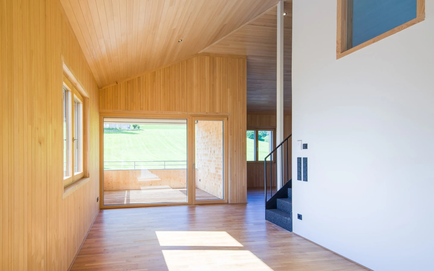 Moderner Wohnraum mit Holzverkleidung an Wänden und Decken, großen Fenstern, Balkon und Treppe, in der Wohnanlage Schwarzen, Alberschwende.