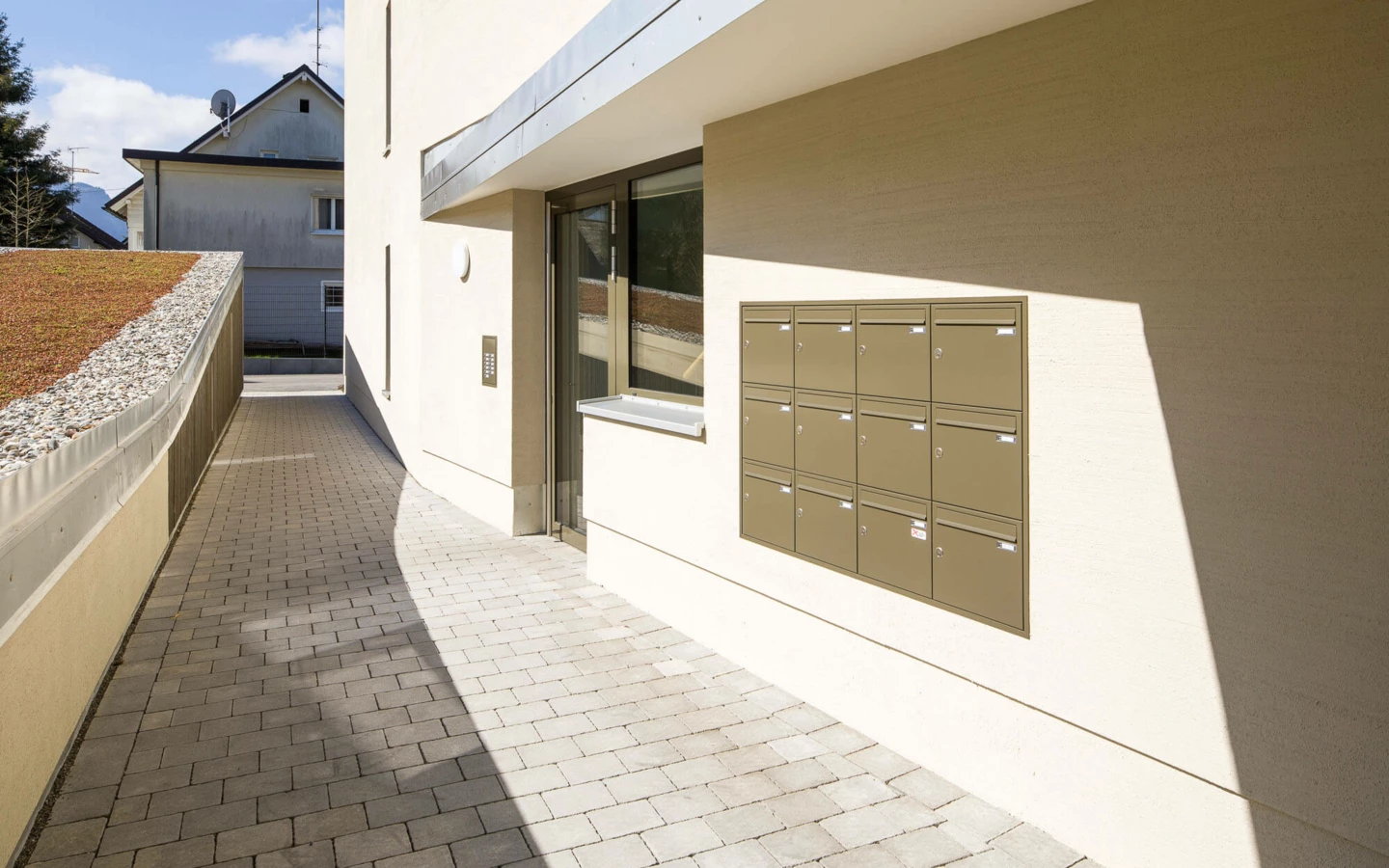 Eingangsbereich der Wohnanlage Feldgasse in Dornbirn mit Briefkästen, Gegensprechanlage und gepflastertem Gehweg