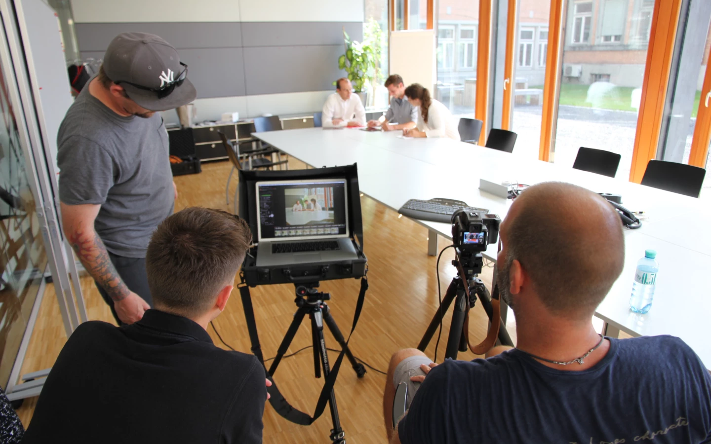 Eine Gruppe von vier Personen filmt eine Besprechung in einem modernen Büro und verwendet dafür professionelle Fotoausrüstung.