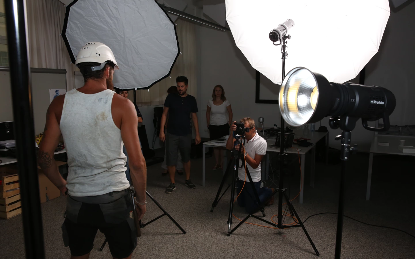 Ein Fotoshooting im Innenbereich mit einem Mann in Bauarbeiterkleidung als Model und Personen an Kameras und Beleuchtung