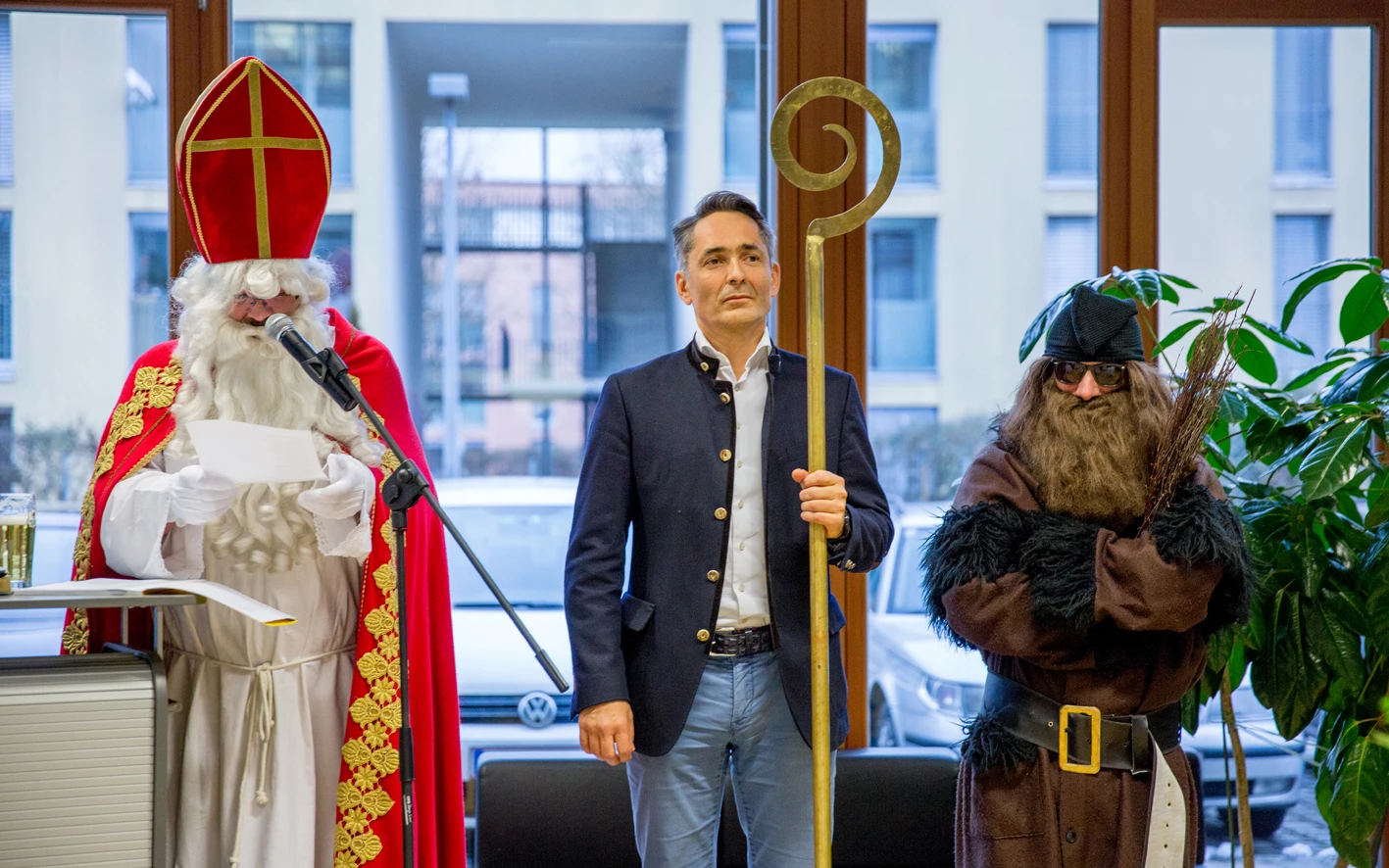 Ein Mann im Nikolauskostüm spricht ins Mikrofon, neben ihm stehen ein Mann im Blazer und ein Knecht Ruprecht (Hubert, Geburtstag).
