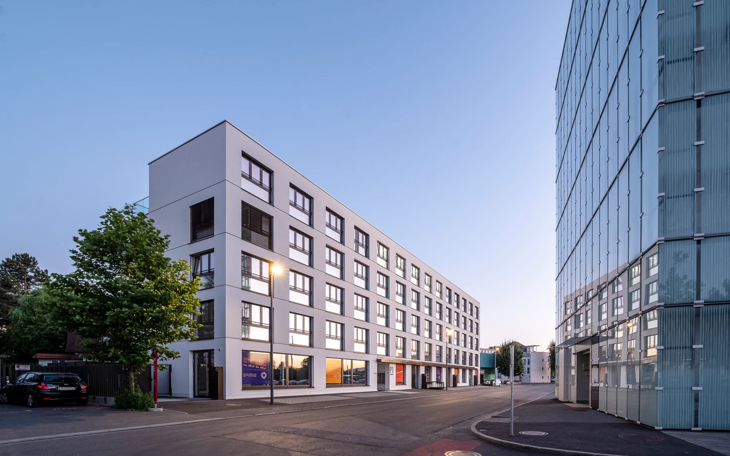 Modernes, weißes Verwaltungsgebäude mit reflektierenden Fenstern und daneben ein verglastes Bürogebäude in Dornbirn.