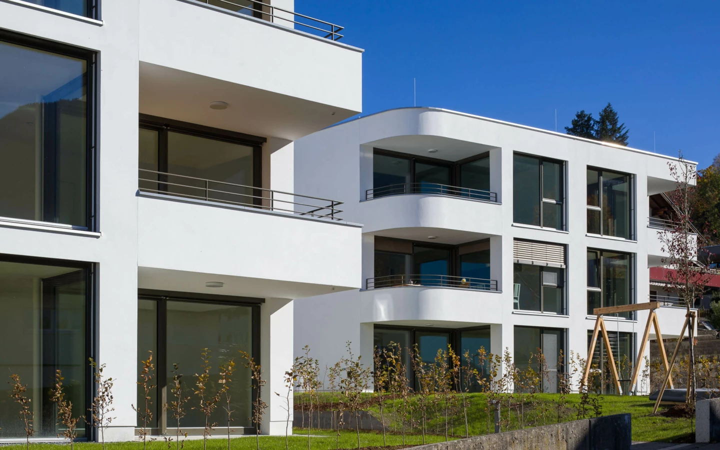 Moderne Wohngebäude mit weißen Fassaden, großen Fenstern und Balkonen unter blauem Himmel in Feldkirch (Wolf-Huber-Straße, Wohnanlage).