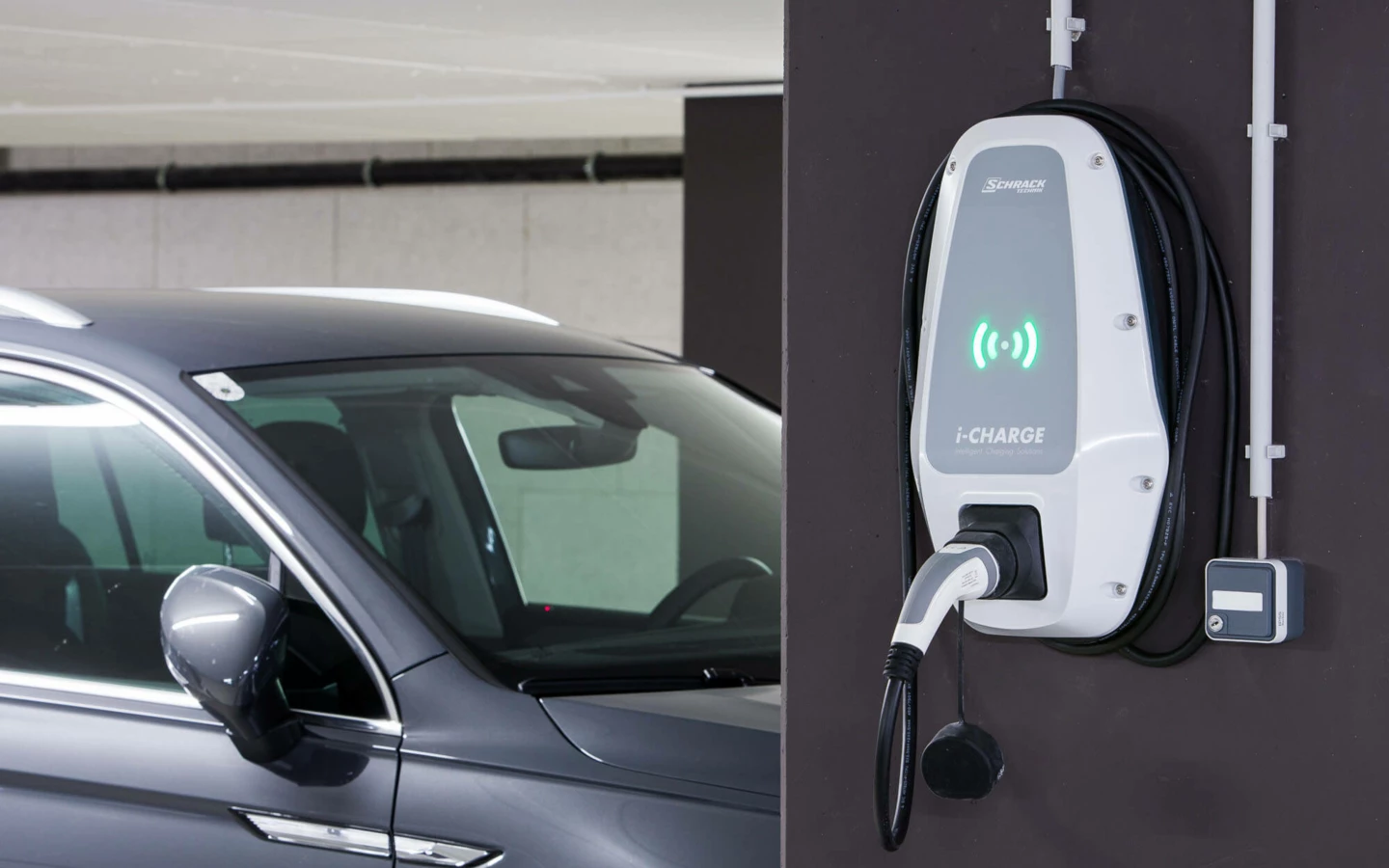 Eine Ladestation für Elektrofahrzeuge der Marke Schrack i-CHARGE an einer Wand neben einem geparkten Auto (Wuhrbaumweg, Wohnanlage).