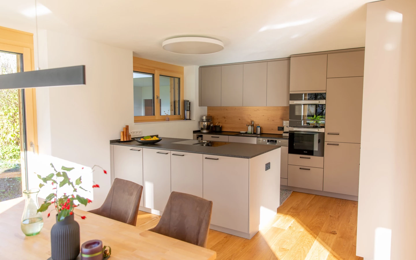 Moderne Küche in einem generalsanierten Einfamilienhaus in Dornbirn mit hellgrauen Fronten, Arbeitsinsel und Holzboden (Generalsanierung, Holzoptik).