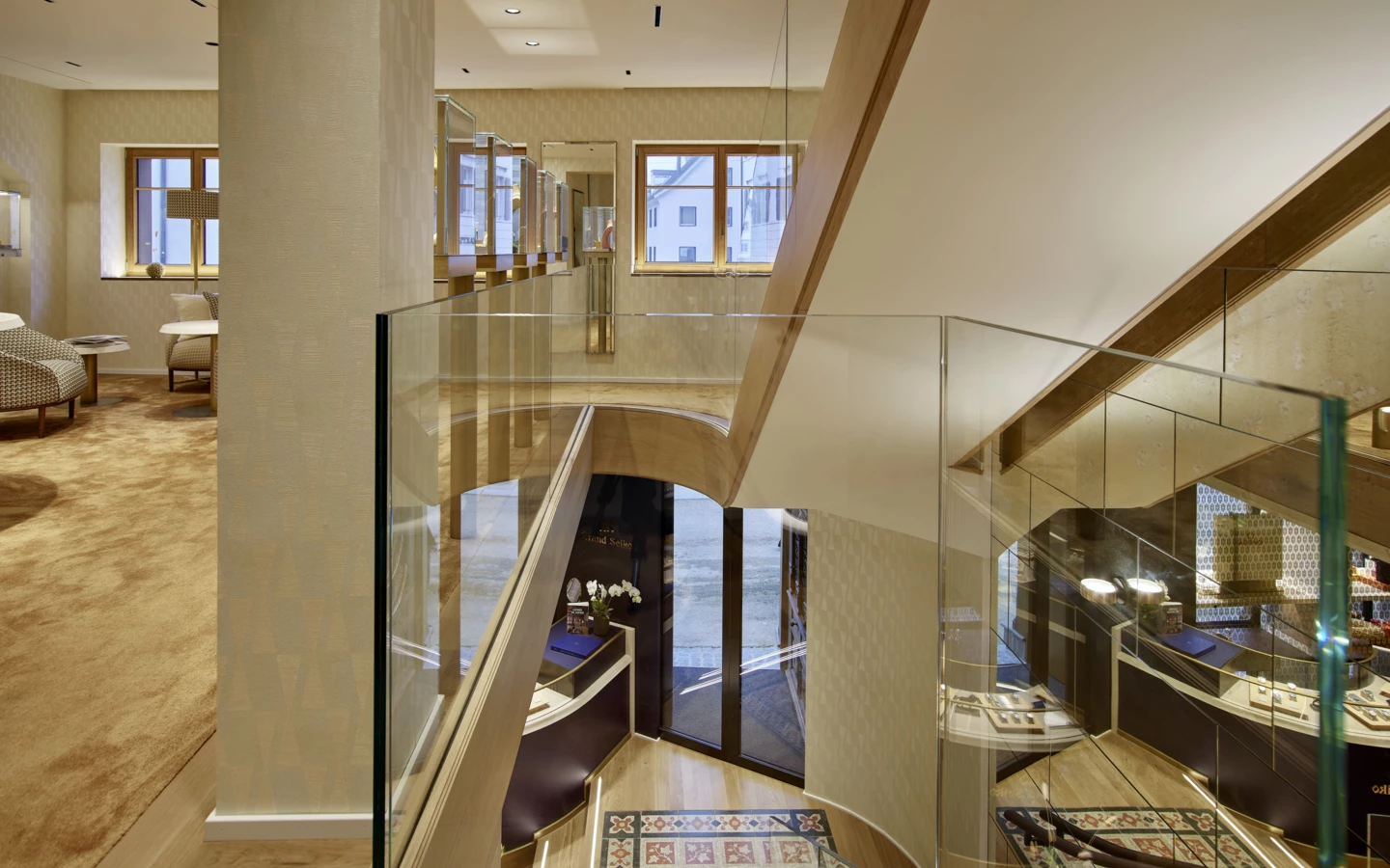 Blick von oben auf eine moderne Holztreppe mit Glasgeländer und eleganten Ausstellungsräumen (Huber, Rathausstr)