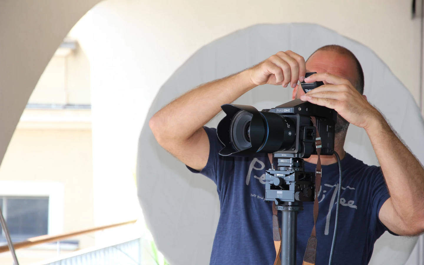 Ein Fotograf mit Glatze und Bart bedient eine professionelle Phase One-Kamera, die auf einem Stativ montiert ist.