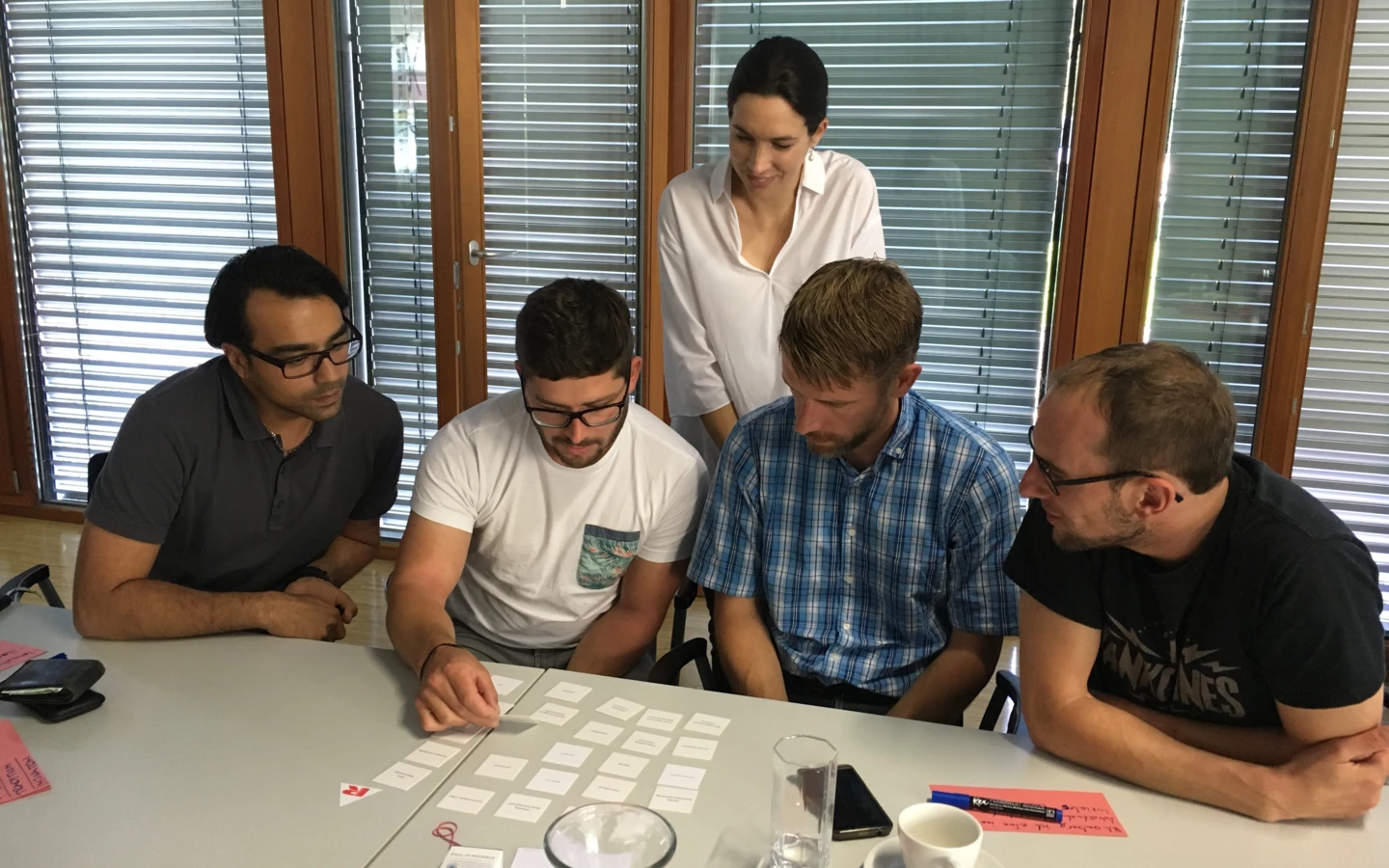 Fünf Personen, darunter eine Frau und vier Männer, arbeiten konzentriert an einem Tisch mit vielen weißen Karten und roten Notizen (Workshop).