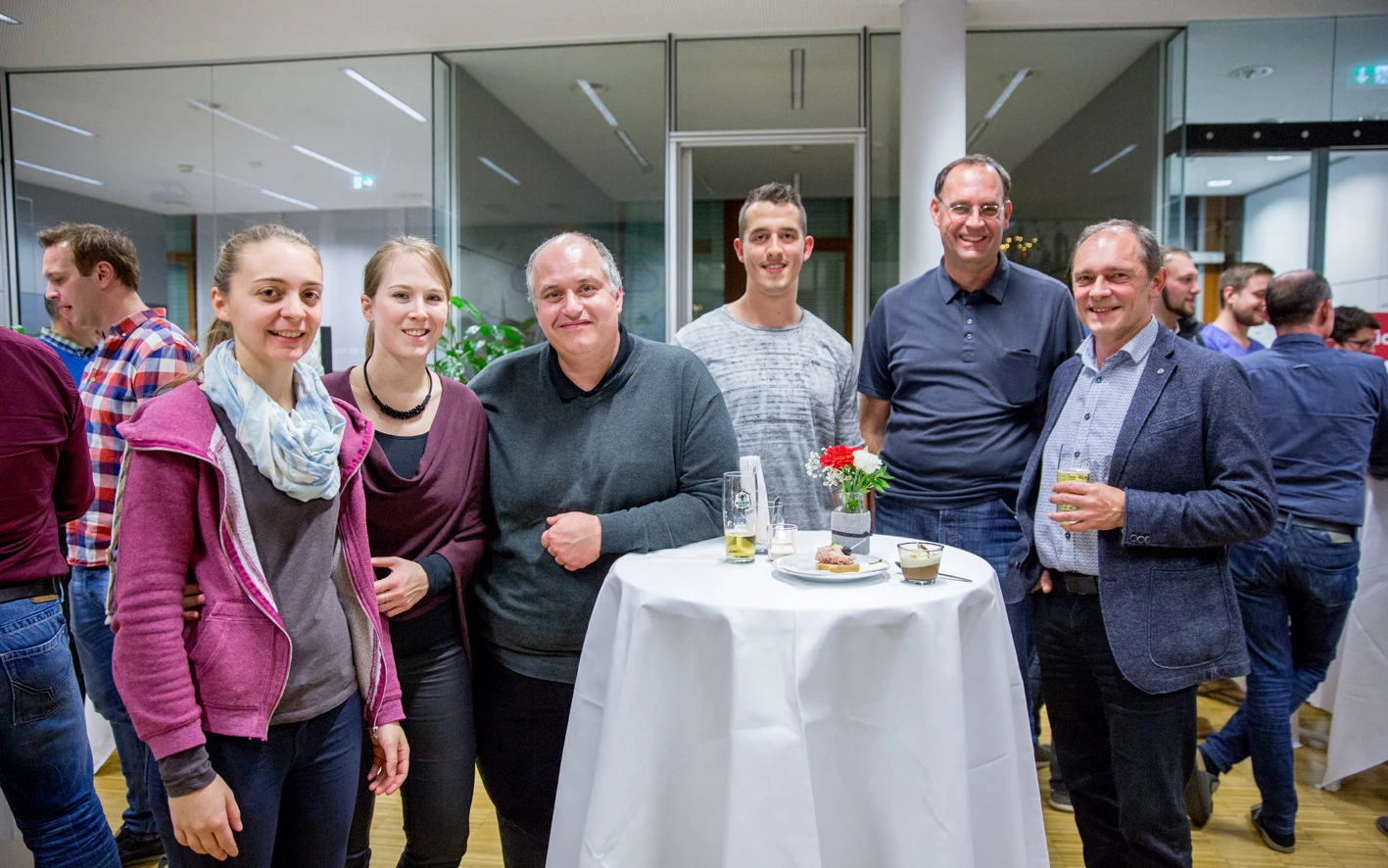 Eine Gruppe von Kollegen steht lächelnd an einem Stehtisch bei einer Veranstaltung von Rhomberg Bau (Hubert, Geburtstag).