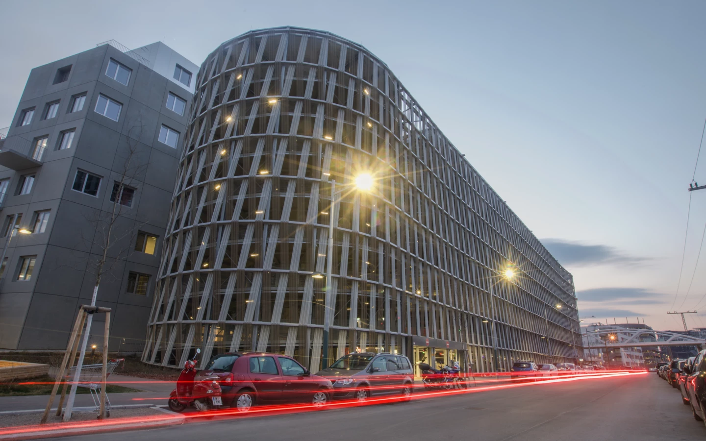 Hochgarage am Wiener Hauptbahnhof bei Abenddämmerung mit dynamischen roten Lichtspuren von vorbeifahrenden Autos (Wien).
