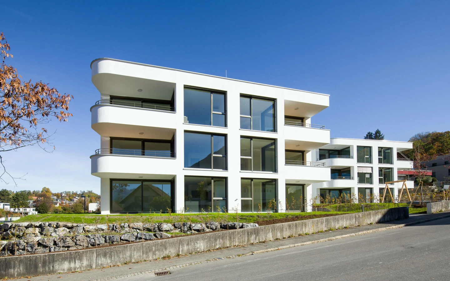 Moderne weiße Wohnanlage mit großen Fenstern und Balkonen unter blauem Himmel in Feldkirch (Wolf-Huber-Straße).