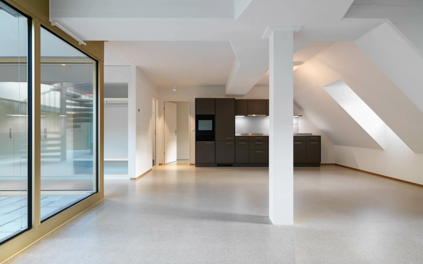 Eine moderne, leere Küche mit dunklen Schränken und einem Backofen in einem hellen Raum mit Dachschrägen und einem breiten Fenster (Multergasse, Gallen).