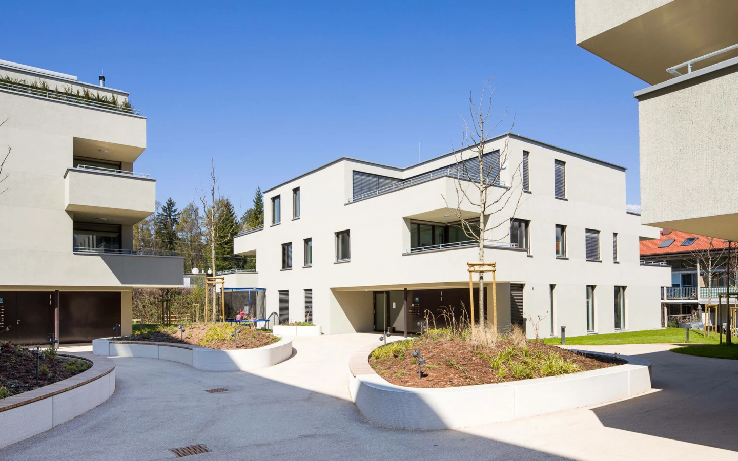Moderne Wohnanlage mit beigen Gebäuden, Balkonen, begrünten Dachterrassen und gepflasterten Wegen unter blauem Himmel (Wuhrbaumweg).