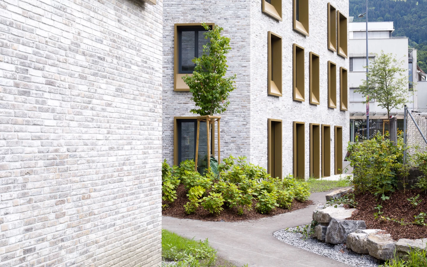 Umfassungsmauer und modernes Gebäude aus hellen Ziegeln an der Kreuzgasse Dornbirn mit Goldfenstern und einem gepflegten Garten