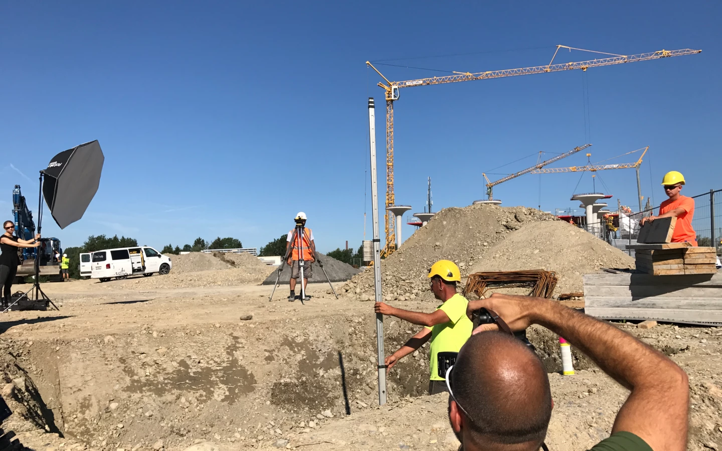 Team bei einem Fotoshooting auf einer Baustelle mit Kranen und Erdhügeln unter blauem Himmel
