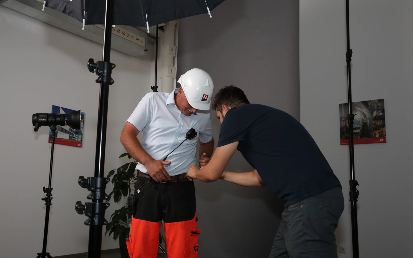 Zwei Männer bei einem Fotoshooting. Einer der Männer trägt Arbeitskleidung von Rhomberg Bau und einen Schutzhelm.