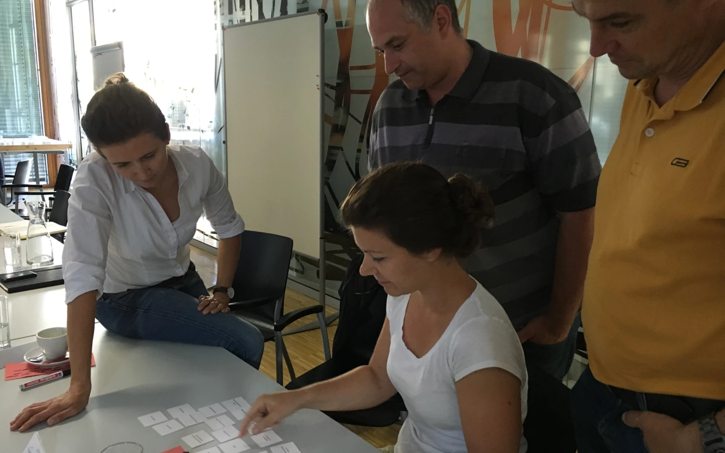 Vier Personen, zwei Frauen und zwei Männer, nehmen an einem Workshop teil und sortieren Karten auf einem Tisch.