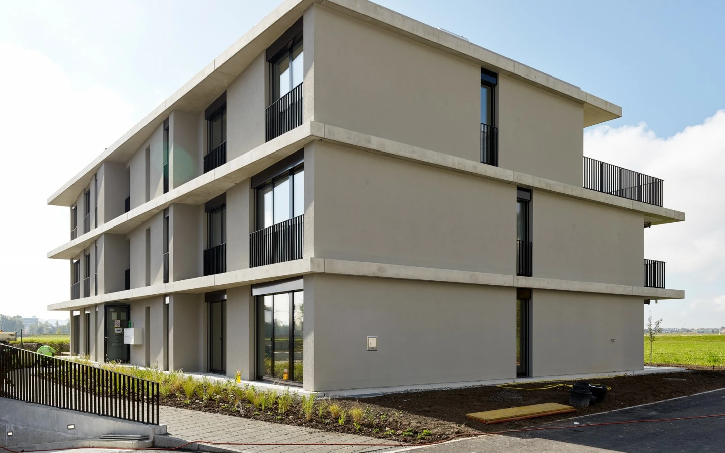 Moderne, mehrstöckige Wohngebäude in Egerkingen mit grauer Fassade, Balkonen und umliegender Grünfläche an einem sonnigen Tag.