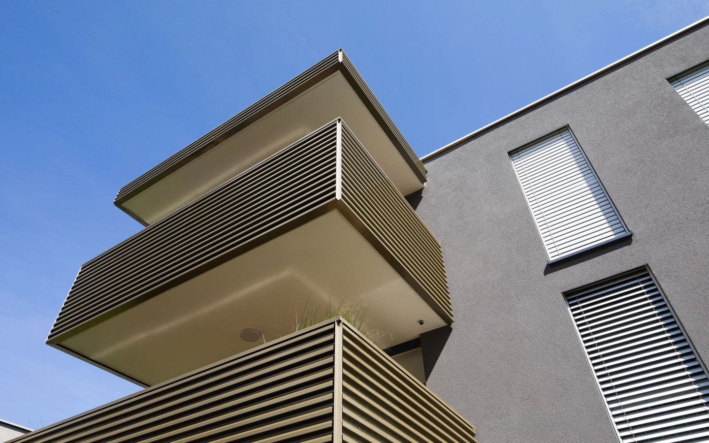 Moderne Wohnanlage in Vandans mit mehrstöckigen Balkonen und grauer Fassade unter blauem Himmel (Bahnhofstraße, Bahnhofsstrasse, Balkonanlage)