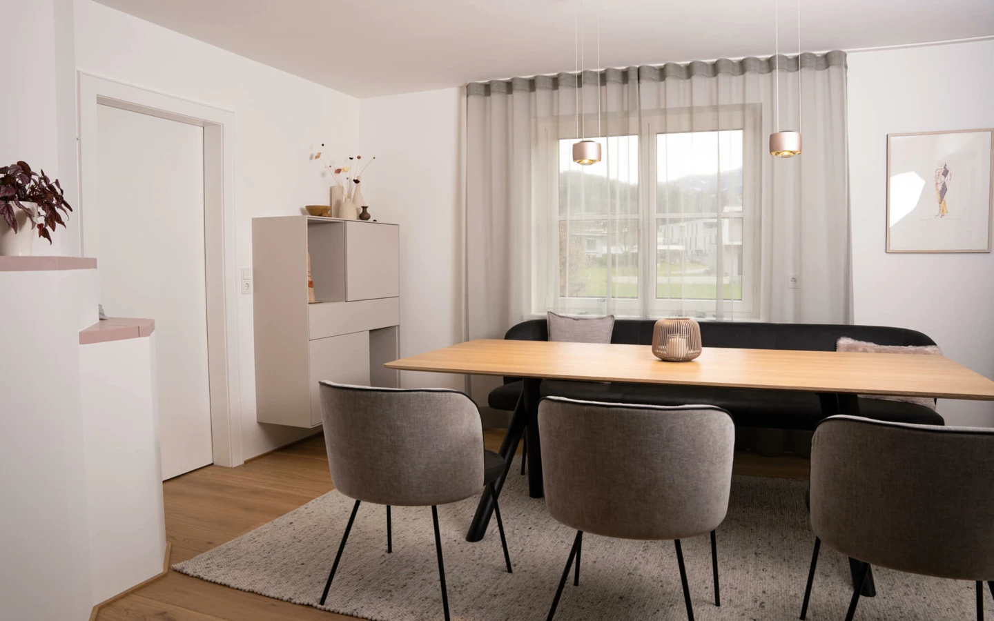 Modernes Esszimmer in einem Einfamilienhaus mit Holztisch, schwarzer Eckbank und grauen Stühlen. Helle Wandfarbe und ein Fenster lassen viel Licht herein (Generalsanierung, Bohle).