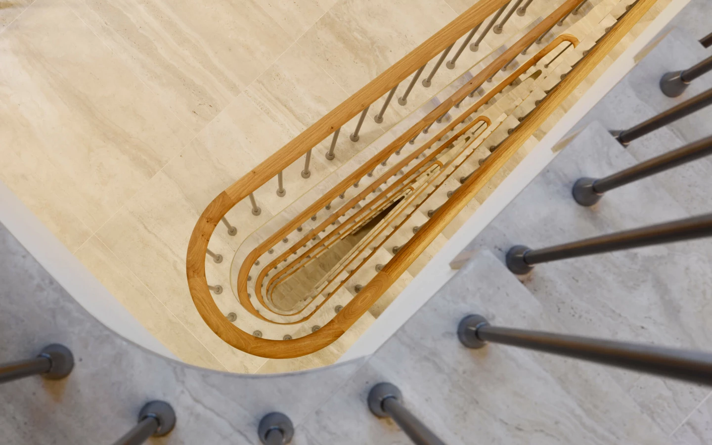 Blick von oben auf eine spiralförmige Treppe aus hellem Marmor mit Holzhandlauf und Metallgeländer im Gebäude Multergasse in St. Gallen.