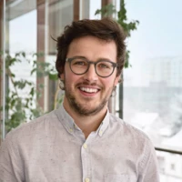 Christoph Erhart lächelt in die Kamera, im Hintergrund Bürofenster mit Blick auf verschneite Häuser und grüne Pflanzen.