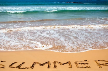 Das Wort "SUMMER" ist in den Sand am Strand geschrieben, mit Meereswellen im Hintergrund.
