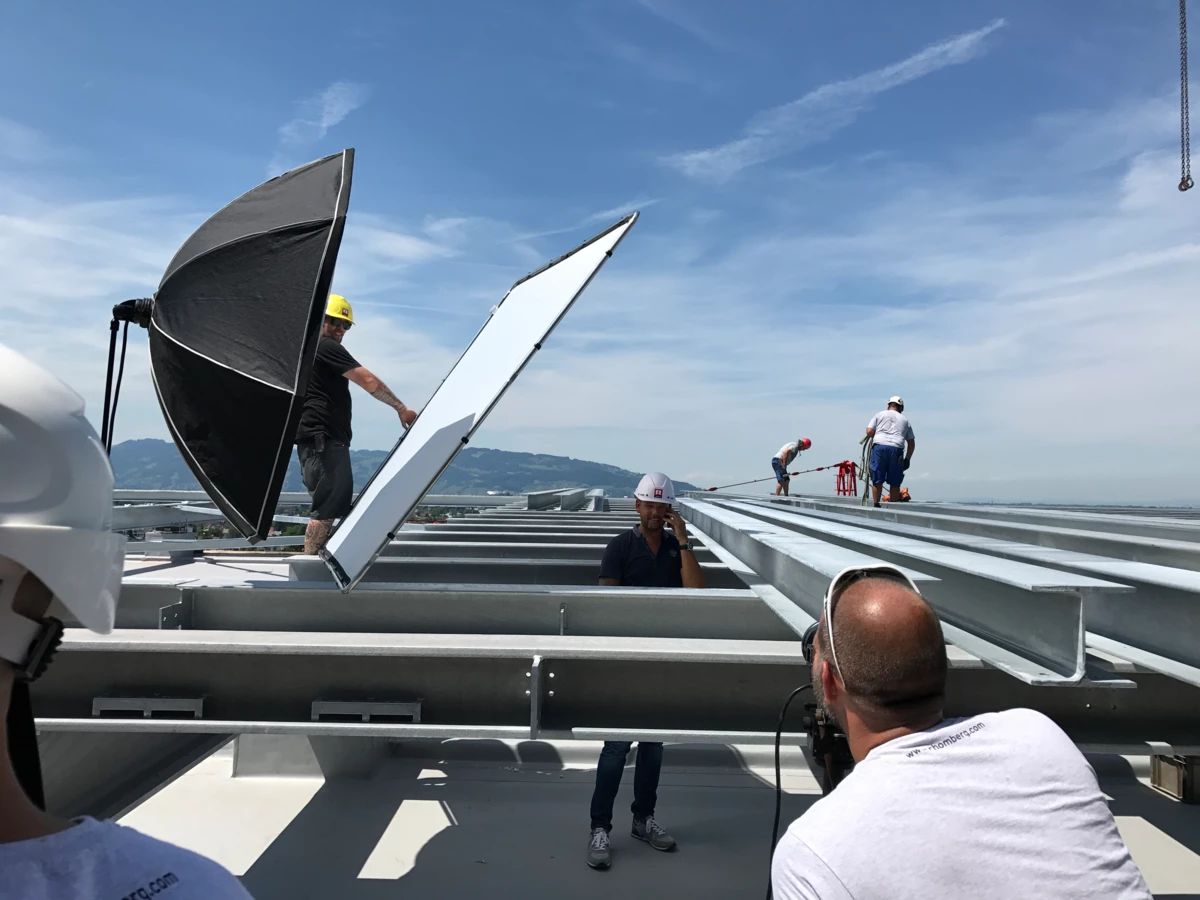 Ein Fotoshooting auf dem Dach eines Gebäudes von Rhomberg Bau GmbH, mit Mitarbeitern und Ausrüstung wie Reflektoren und Blitzschirmen.