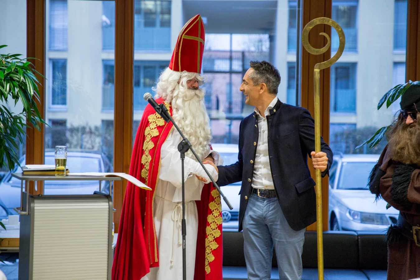 Ein lächelnder Mann im Trachtenjanker schüttelt dem Nikolaus mit Bischofsmütze, rotem Mantel und weißem Bart die Hand (Hubert, Geburtstag).