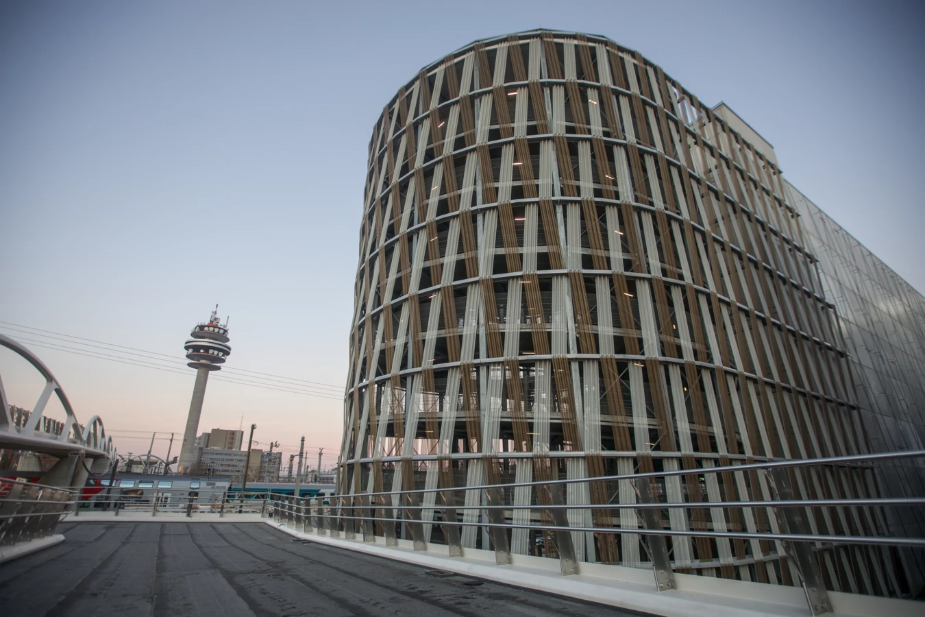 Gerundete Hochgarage am Wiener Hauptbahnhof mit einem Fernmeldeturm und Bahnsteigen im Hintergrund (Wien).