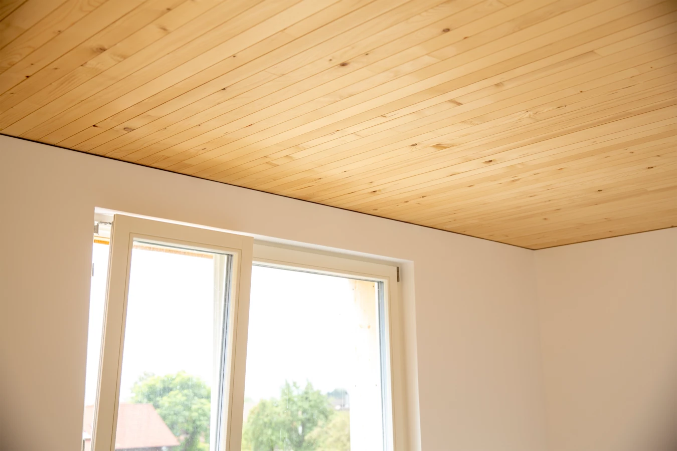Natürliche Holzdecken in Innenräumen mit einem Fenster, das auf eine grüne Landschaft blickt, Neubau Hellbrunnerstraße (Hellbrunnenstraße).