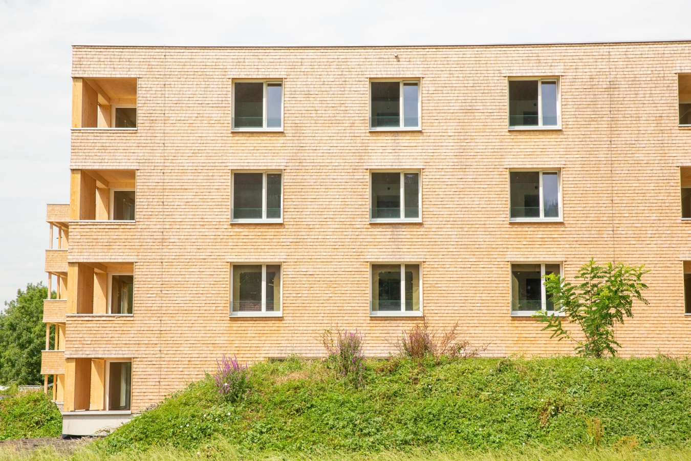 Mehrstöckiges Holzgebäude mit Holzschindelfassade, Fenstern und Balkonen, umgeben von grüner Vegetation an der Hellbrunner Straße (Hellbrunnenstraße).