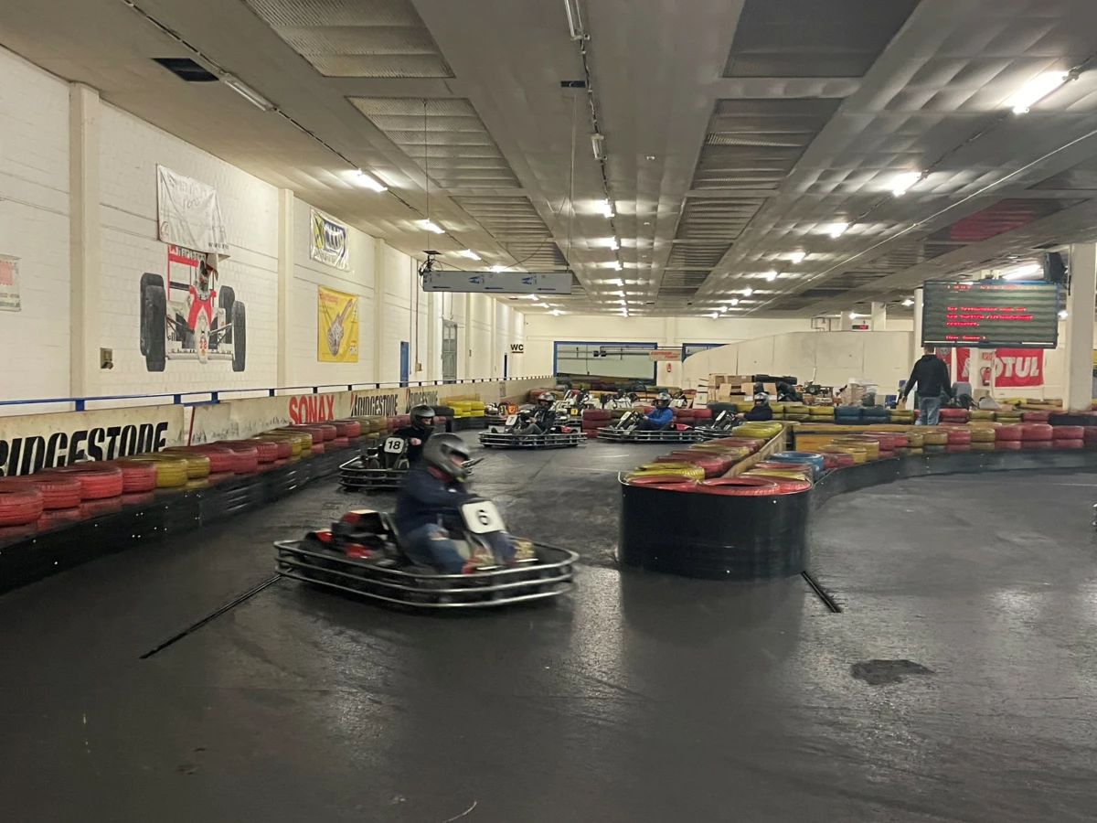 Mehrere Personen in Gokarts fahren auf einer Indoor-Rennstrecke mit Reifenbegrenzungen und Werbebannern an den Wänden (Lehrlingsabend).