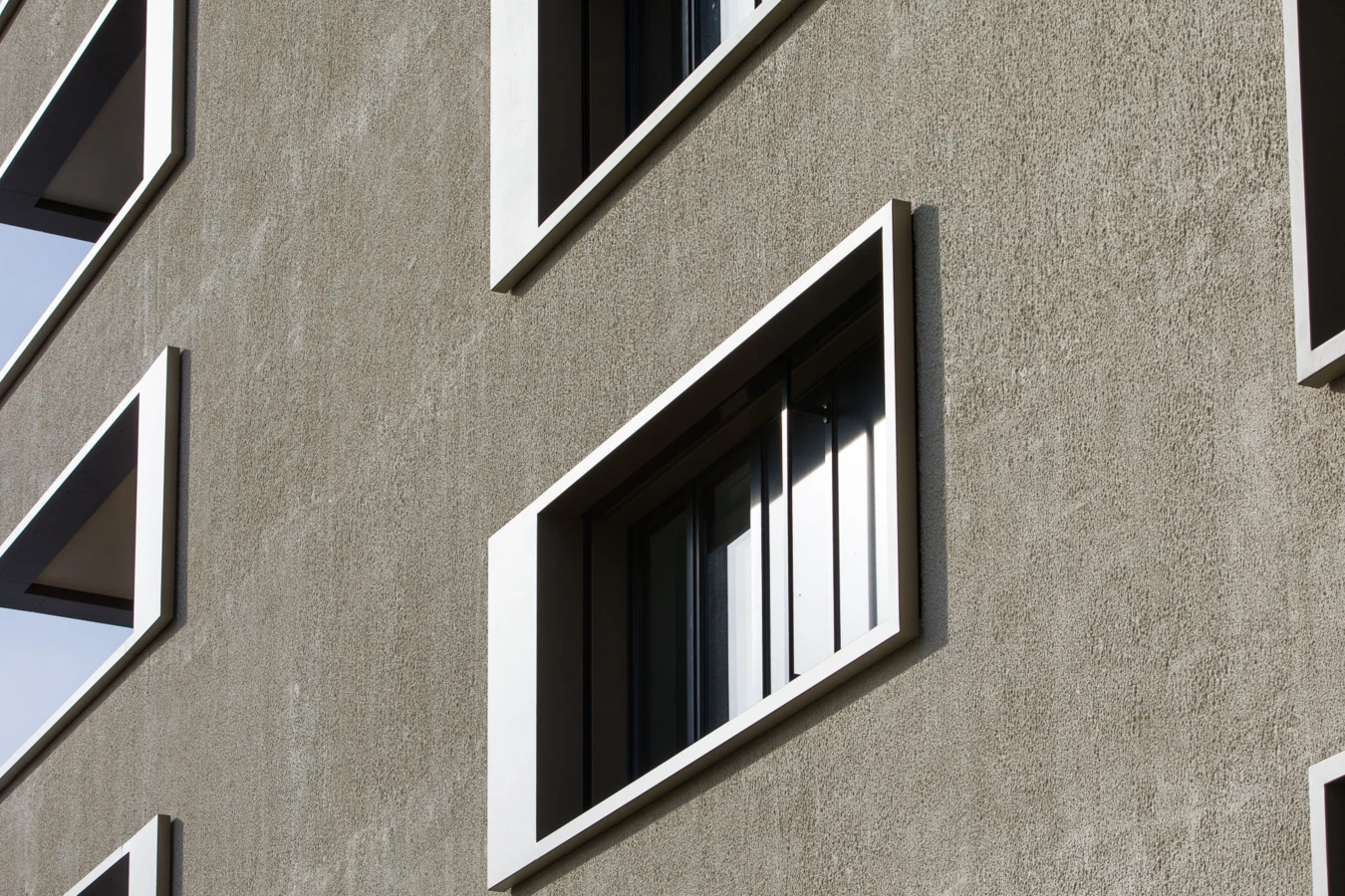 Fassade eines modernen Gebäudes mit strukturiertem Putz und schrägen Fenstern mit weißen Rahmen (Bäumleareal)