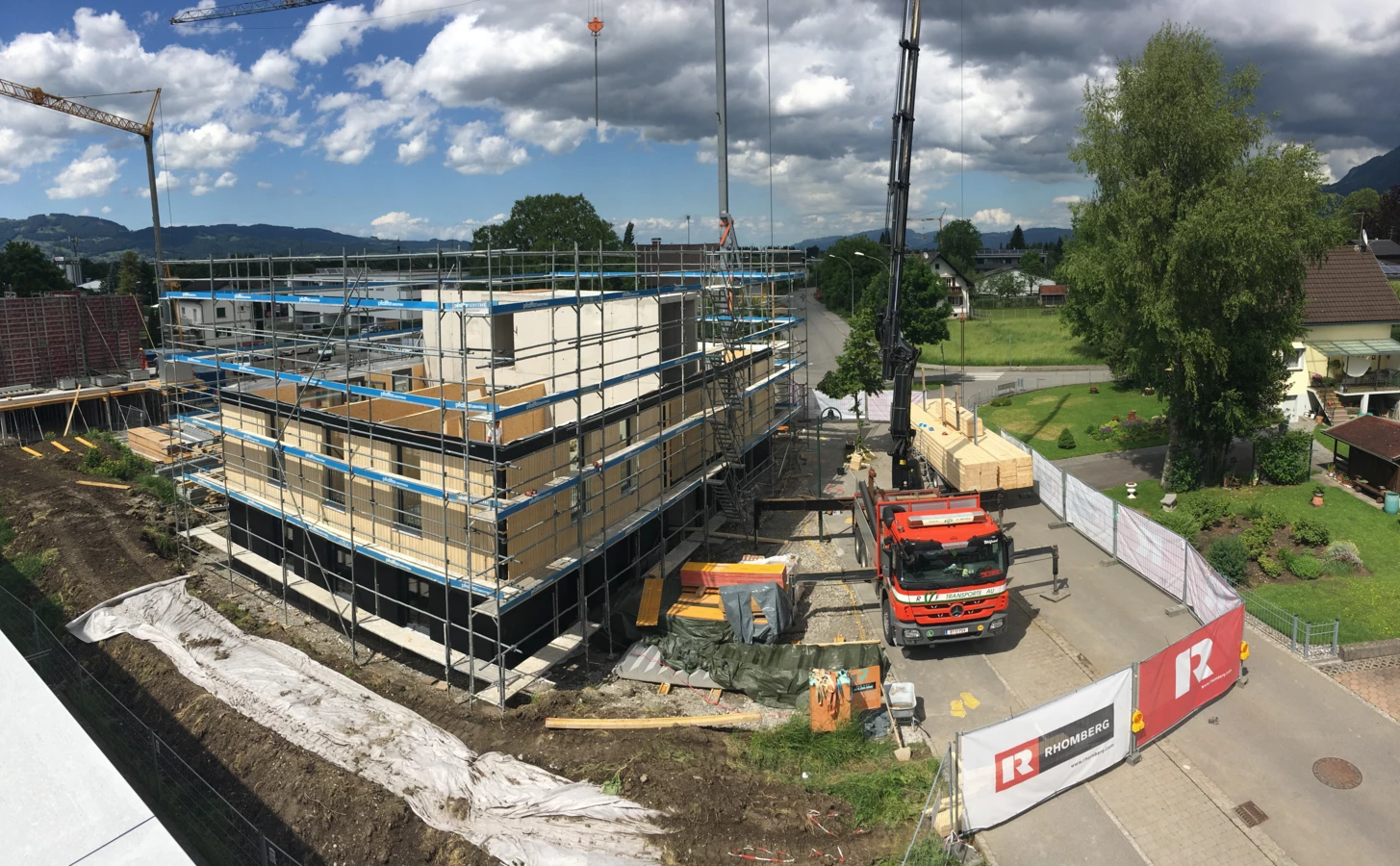 Holzbau-Projekt von Rhomberg Bau mit Gerüst, Baukran und Lieferwagen unter blauem Himmel mit Wolken (Architekturexkursionen, Holzbauprojekte).