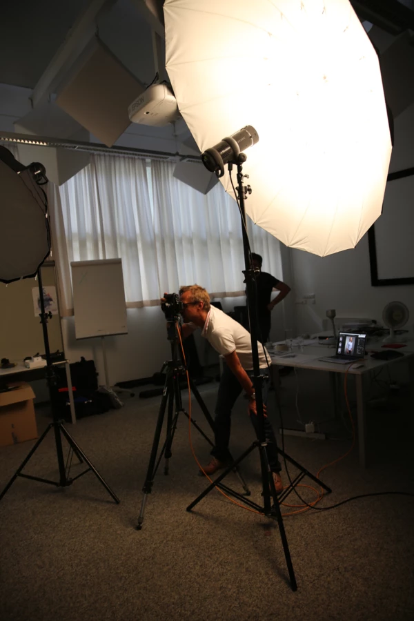 Ein Fotograf mit Brille fotografiert im Studio, umgeben von zwei Softboxen und einem Laptop mit Bildvorschauen.