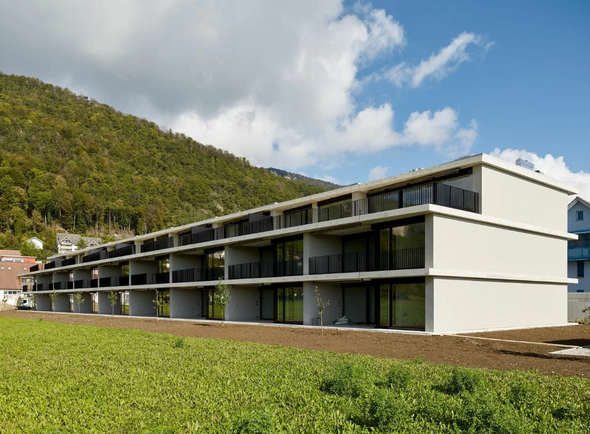 Moderne, mehrstöckige Wohnanlage in Egerkingen mit Balkonen, umgeben von einem grünen Feld und bewaldeten Hügeln unter blauem Himmel.