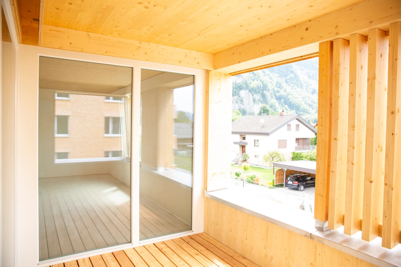Blick von einem Balkon aus Holz mit Glasschiebetüren auf ein Wohngebiet mit Häusern und einer bergigen Landschaft im Hintergrund (Hellbrunnenstraße).